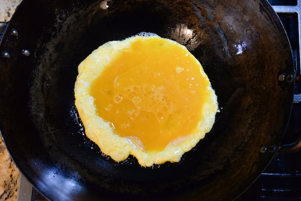 A close-up shot of an oiled wok holding loose, custardy beaten eggs.
