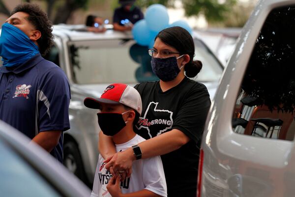 FILE - In this Thursday, May 21, 2020 photo, Vanessa Romero holds her son at a memorial service for the 23rd victim of the Aug. 3 Walmart shooting while wearing an "El Paso Strong" T-shirt and a face mask in El Paso, Texas. AP Photo/Cedar Attanasio, File)