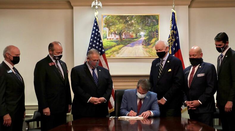 Gov. Brian Kemp signs the elections overhaul into law at the Capitol, flanked by legislative leaders.