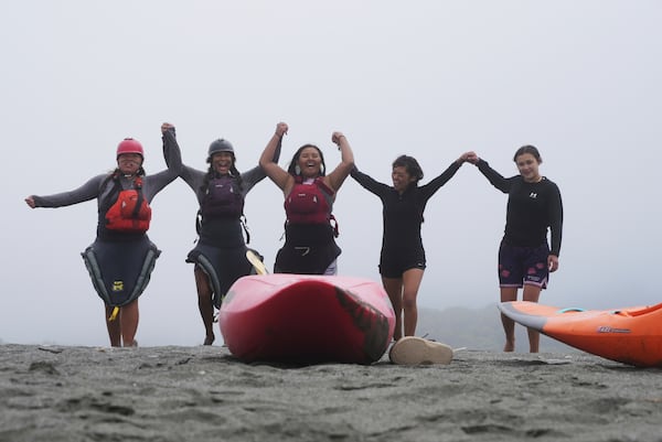 Young native paddlers hold hands and cheer as they walk across a sandy stretch that separates the Klamath River from the Pacific Ocean on Friday July 11, 2025, in Klamath, Calif. (AP Photo/Brittany Peterson)
