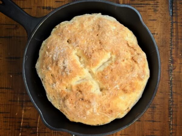 An overhead shot of a fresh-baked loaf of soda bread in a cast iron pan on a wood table.