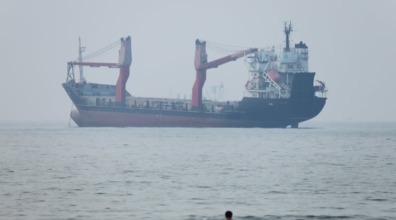 A group of people stands in shallow water as a cargo ship appears anchored in the Strait of Hormuz off Bandar Abbas, Iran, Tuesday, June 30, 2026. (Amirhosein Khorgooi/ISNA via AP)