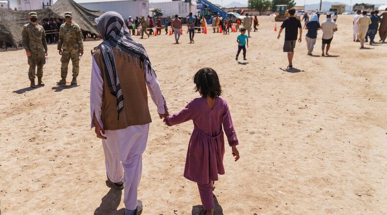 FILE - A man walks with a child through Fort Bliss' Doña Ana Village where Afghan refugees are being housed, in New Mexico, Friday, Sept. 10, 2021. (AP Photo/David Goldman, File)