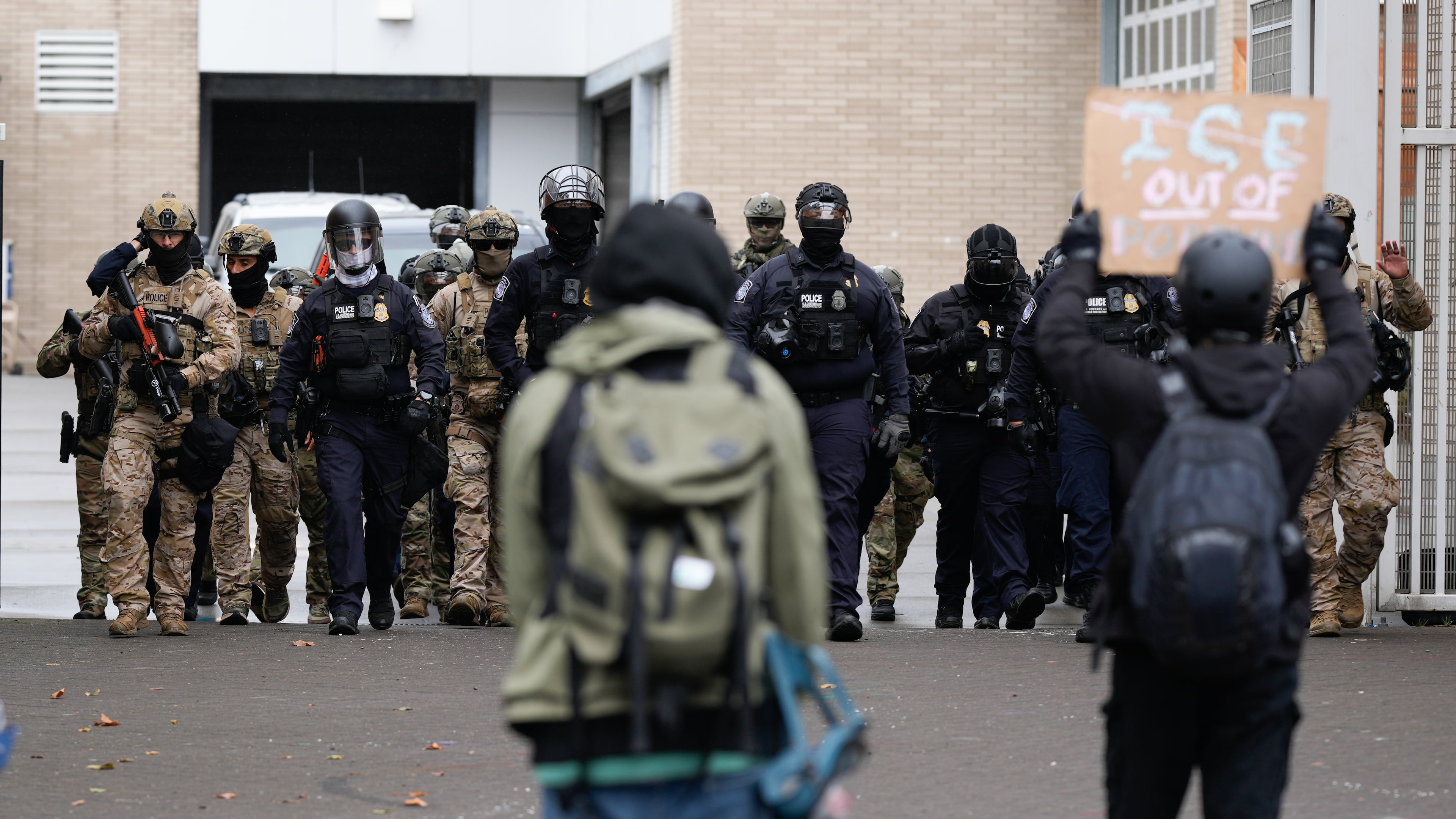 FILE - People protest outside a U.S. Immigration and Customs Enforcement facility as law enforcement officers walk out of the gates to guard vehicles leaving the facility on Oct. 11, 2025, in Portland, Ore. (AP Photo/Jenny Kane, File)