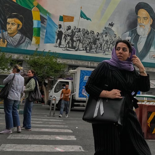 A woman crosses a street in front of a painting of the late Iranian revolutionary founder Ayatollah Khomeini and paramilitary Basij forces in downtown Tehran, Iran, Sunday, May 24, 2026. (AP Photo/Vahid Salemi)