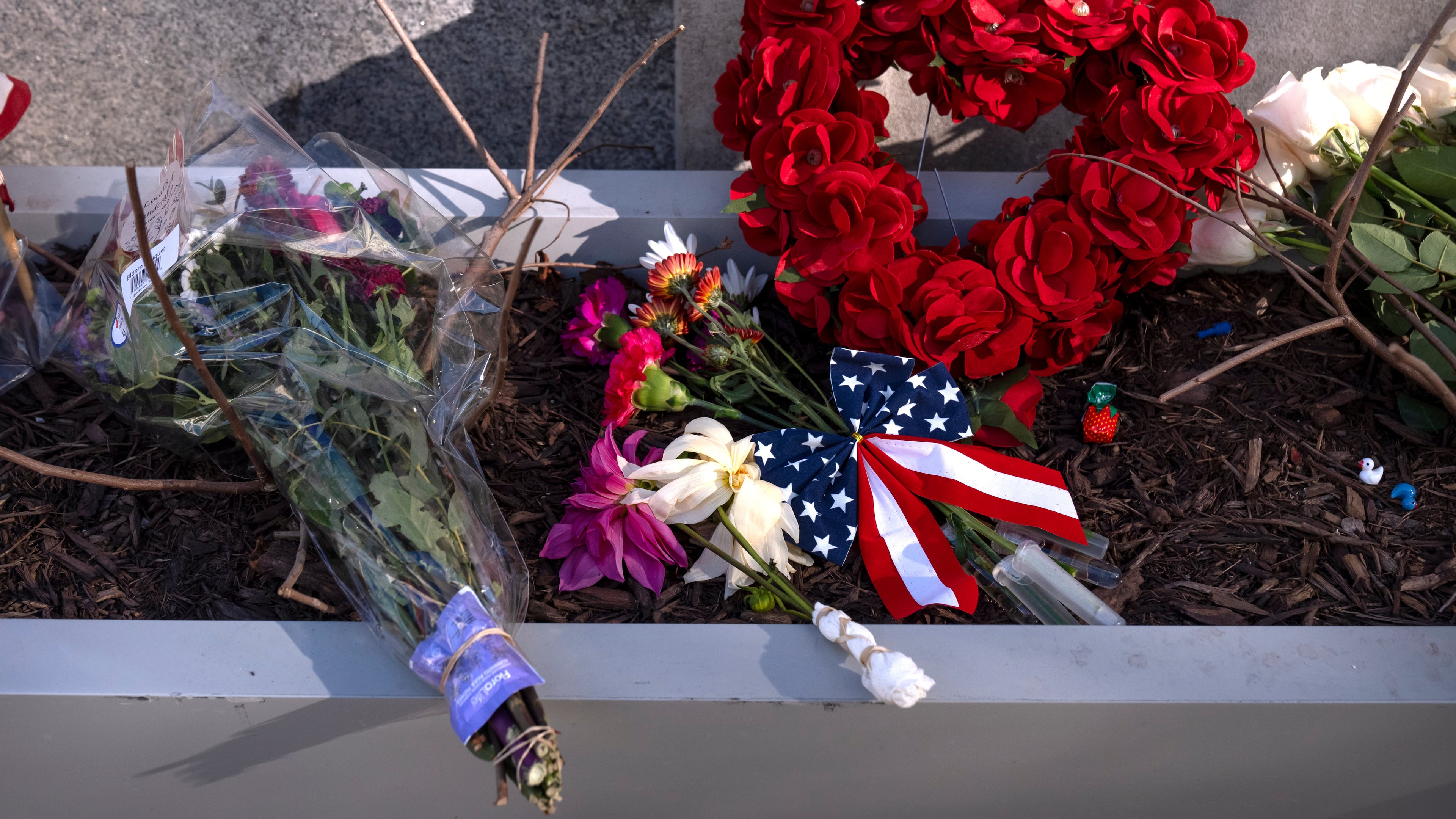 A small memorial of flags, flowers, other items are seen in a planter, Friday, Nov. 28, 2025, near the site where two National Guard members were shot in Washington. (AP Photo/Mark Schiefelbein)