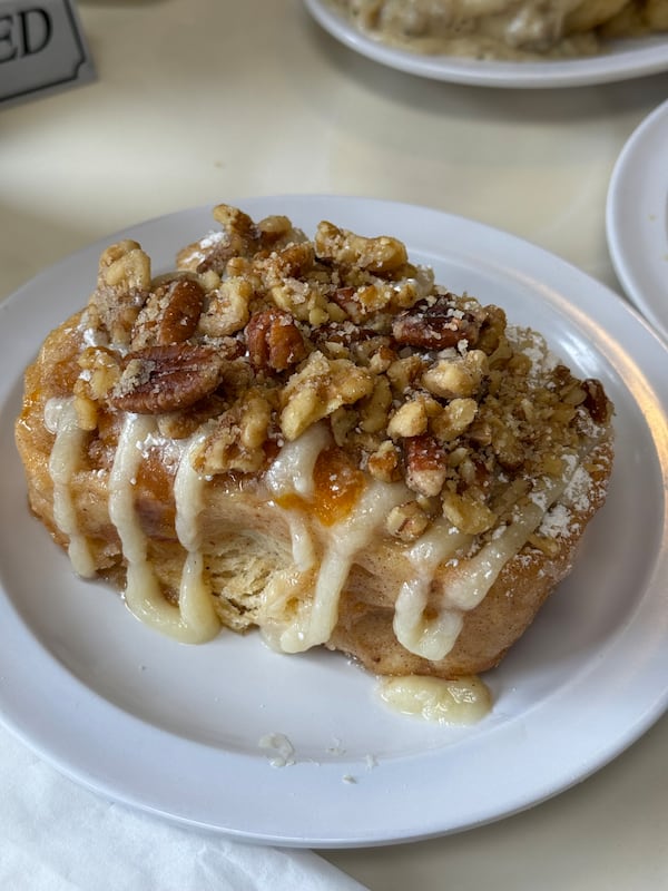 A large sweet roll on a plate covered in chopped nuts and an icing-like sauce