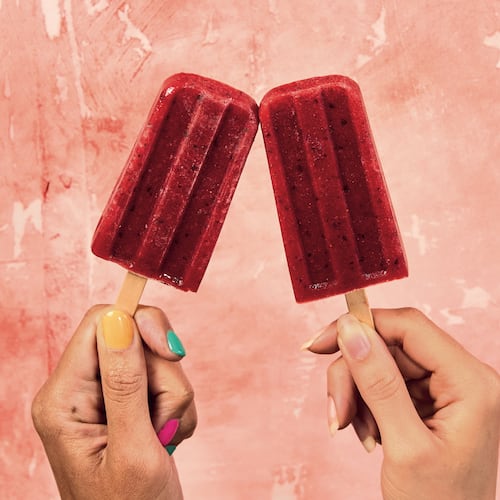 two hands holding one red popsicle each with a pink background