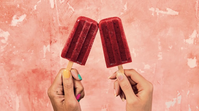 two hands holding one red popsicle each with a pink background