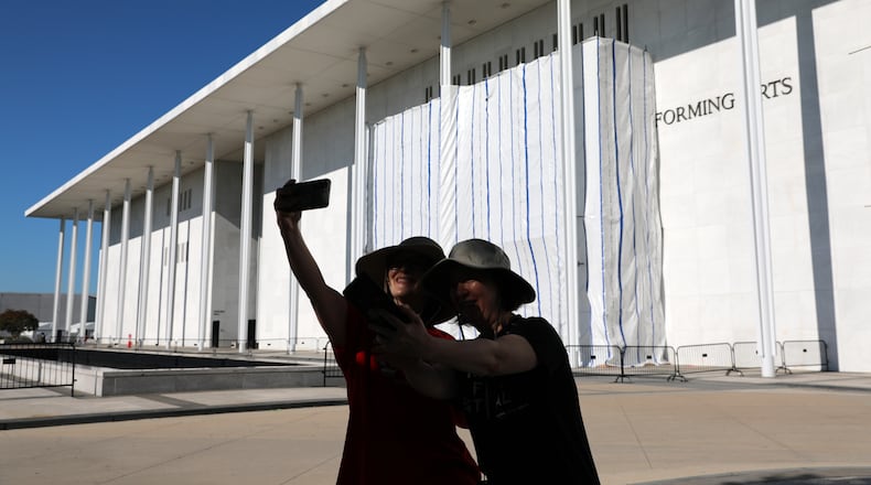 Women take a selfie as the wall of the John F. Kennedy Center for the Performing Arts is covered in tarp as work continues on the removal of President Donald Trump's name, Saturday, June 13, 2026 in Washington. (AP Photo/Rahmat Gul)