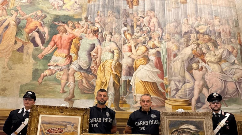 In this picture made available by the Italian Carabinieri in Parma, northern Italy, Friday, Aug. 14, 2026, Carabinieri pose near three paintings recovered following a police operation: "Tasse et plat de cerises" by Paul Cezanne, left, "Odalisque Sur La Terrasse" by Henri Matisse, center, and "Les Poissons" by Pierre Auguste Renoir, right. (Italian Carabinieri via AP)