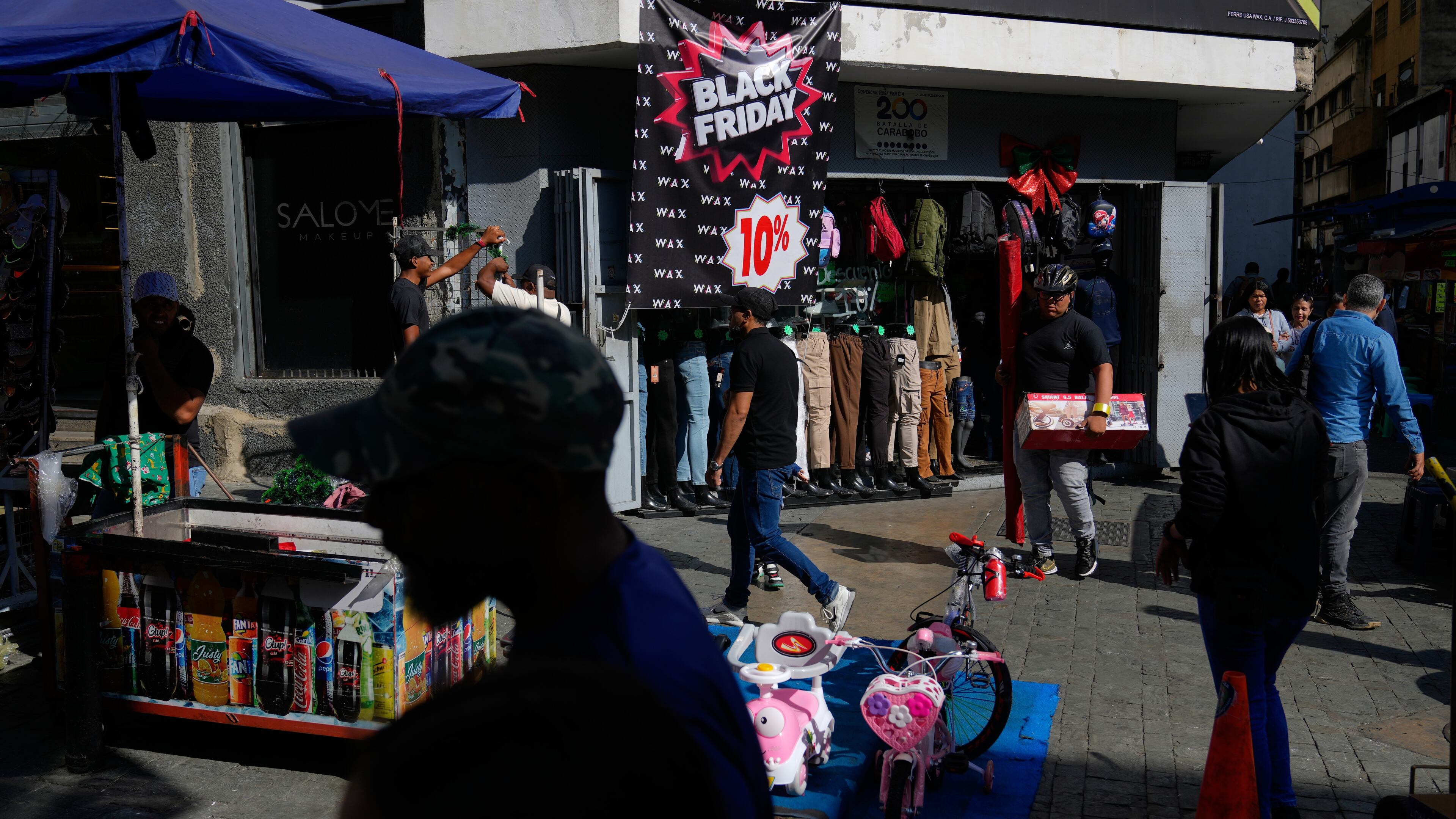 Pedestrians walk past a storefront promoting Black Friday discounts in Caracas, Venezuela, Friday, Nov. 28, 2025. (AP Photo/Ariana Cubillos)