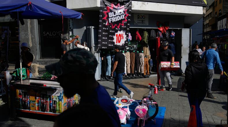 Pedestrians walk past a storefront promoting Black Friday discounts in Caracas, Venezuela, Friday, Nov. 28, 2025. (AP Photo/Ariana Cubillos)