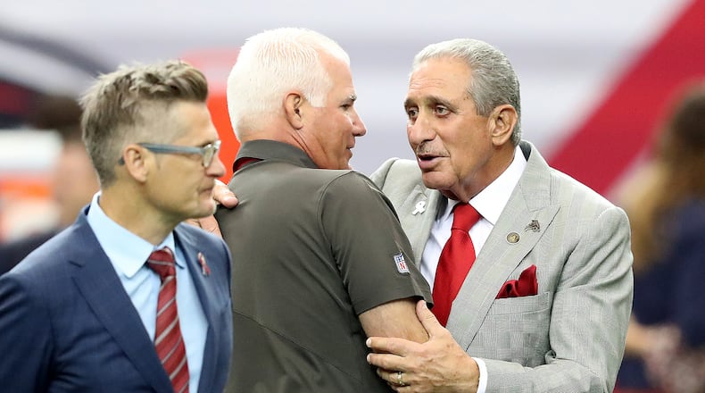 Former Falcons head coach Mike Smith gets a hug from Arthur Blank after speaking with Thomas Dimitroff before Tampa Bay’s game in the Georgia Dome on Sept. 11. Curtis Compton /ccompton@ajc.com
