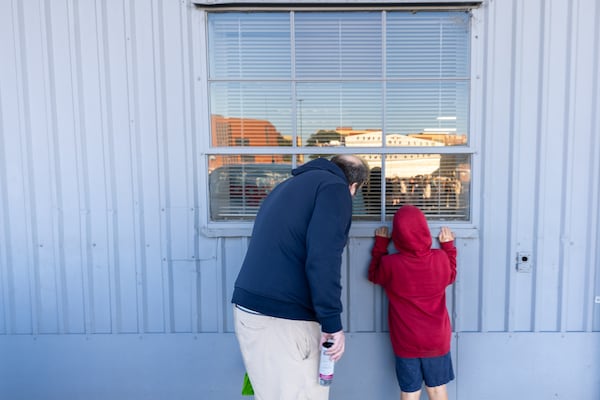 Andrew Williams and his son Terran Bosserman, 9, of Nashville, peek to see the goods before the Delta Flight Museum Surplus Sale in Atlanta on Friday, Oct. 10, 2025. They drove in for the night just for the sale. Every month, Delta fans wait in line for hours for the chance to buy vintage airline merch. (Arvin Temkar/AJC)