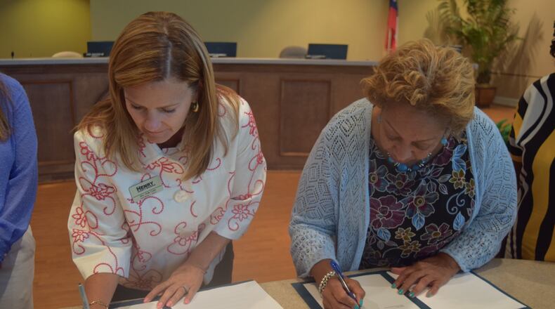 Board of Education chair Holly Cobb and Board of Commissioners chair Carlotta Harrell sign the agreement.