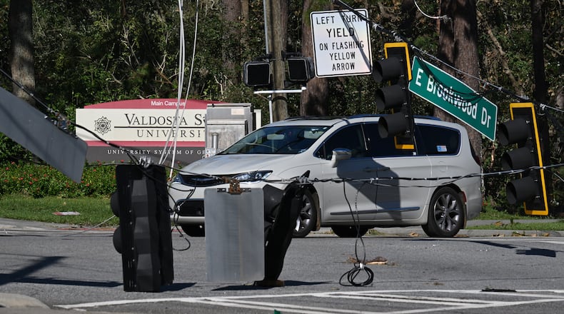 A car drives by fallen traffic signals and wires near Valdosta State University on Saturday, Sept. 28, 2024. The devastation in Valdosta was extensive after the South Georgia city was battered with hurricane-force winds on Helene’s path across the state. Damaging Helene has swept through Georgia, leading to at least 15 deaths. All 159 counties are now assessing the devastation and working to rebuild, even as serious flooding risks linger. (Hyosub Shin/AJC)