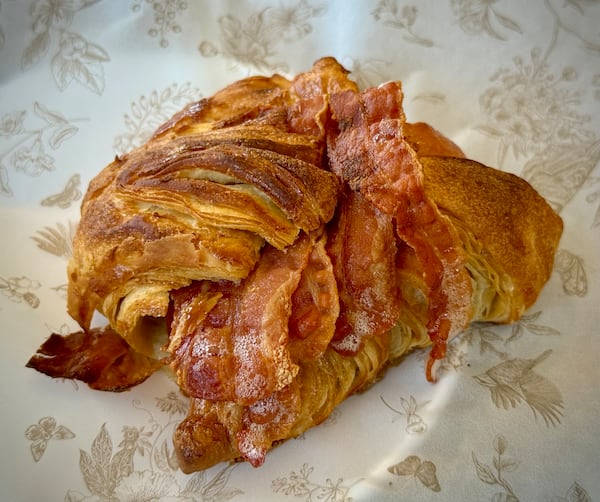A croissant sandwich on paper with bacon peeking out of the middle of the croissant.
