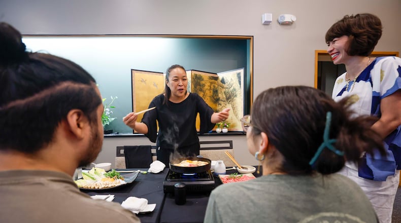 Sachiyo Nakato Takahara, owner of Nakato Japanese Restaurant, happily explains to students what the “Sukiyaki” dish is made of as Freedom University executive director Laura Emiko Soltis looks on during a celebratory dinner at Nakato restaurant in Atlanta on Sunday, Aug. 23, 2026, marking the conclusion of the virtual study abroad Japan program. (Miguel Martinez/AJC)