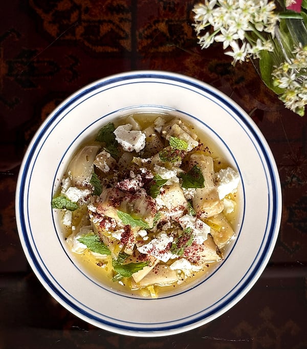 An overhead view of a plate of oil-cured eggplant cut into baton-like segments and garnished with feta cheese and herbs.