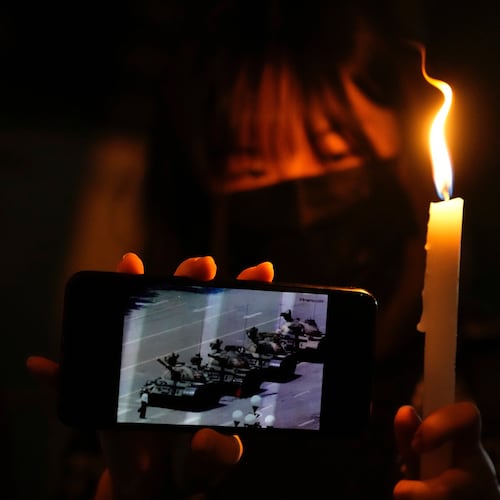 FILE -A woman holds up a candle and an image of a man facing off tanks to mark the anniversary of the military crackdown on a pro-democracy student movement in Beijing, during a light candle vigil outside Victoria Park in Hong Kong, Friday, June 4, 2021. (AP Photo/Kin Cheung, File, File)