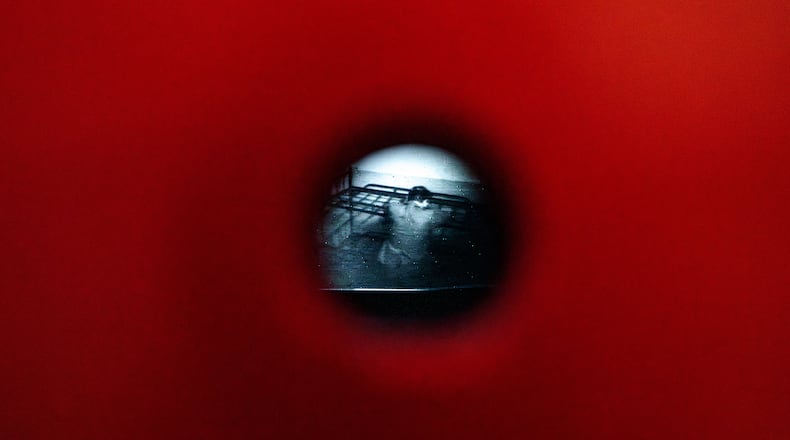 A video from the Communist era secret police surveillance archives, seen through a pinhole, shows Anton Uncu sitting on a metal bed, a day before the opening of the "A.REST 1989 — The Securitate Video Archive" exhibition, at the National History Museum of Romania, in Bucharest, Romania, Monday, June 15, 2026. (AP Photo/Andreea Alexandru)