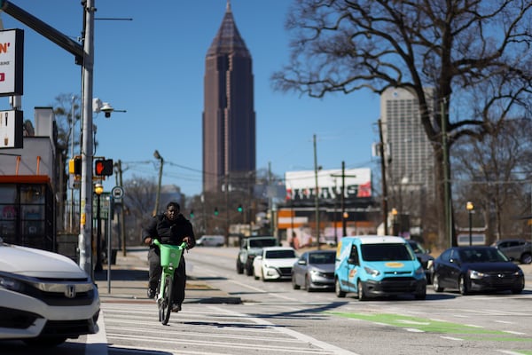 The Bank of America Plaza building is shown in the background as a bicyclist and automobiles prepare to travel on Ponce De Leon Ave at the intersection of Ponce De Leon Ave and Monroe Dr NE, Friday, Feb. 21, 2025, in Atlanta. This intersection is one of several that are slated for upgrades under the Moving Atlanta Forward infrastructure bond to complete street projects. Currently, residents cross the streets in potentially dangerous manners, and the sidewalks are damaged or incomplete. (Jason Getz/AJC)
