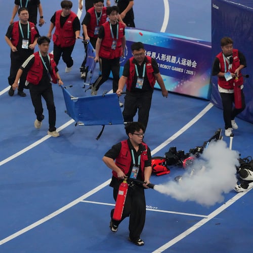 Officials extinguish a fire of a Humanoid robot after hitting the barrier at the end of the 100 meter final race during the World Humanoid Robot Games in Beijing, Wednesday, Aug. 26, 2026. (AP Photo/Achmad Ibrahim)