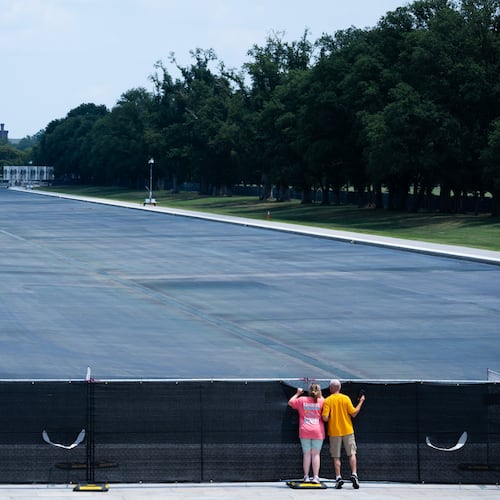 Individuals peek over the fence to see the drained Lincoln Memorial Reflecting Pool,, Monday, July 27, 2026, in Washington. (AP Photo/Allison Robbert)