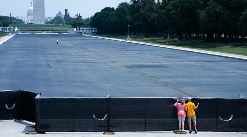 Individuals peek over the fence to see the drained Lincoln Memorial Reflecting Pool,, Monday, July 27, 2026, in Washington. (AP Photo/Allison Robbert)