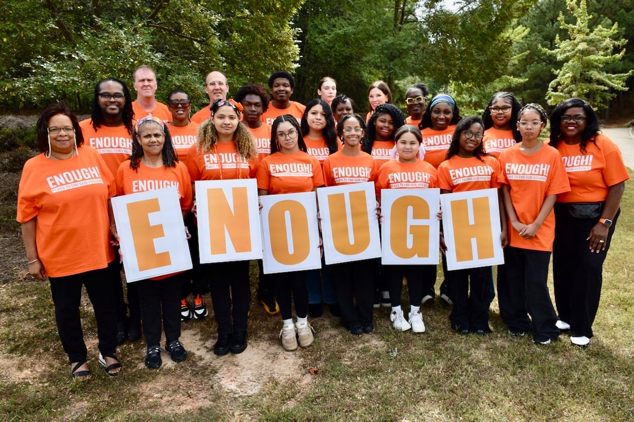 A group of peer advocates and volunteers at Atlanta's Jared's Heart of Success hold up an Enough sign during a play-reading event to confront gun violence on Saturday. Jared's Heart of Success is a nonprofit started by Sharmaine Brown, who lost her son to a stray bullet in 2015. (Courtesy)