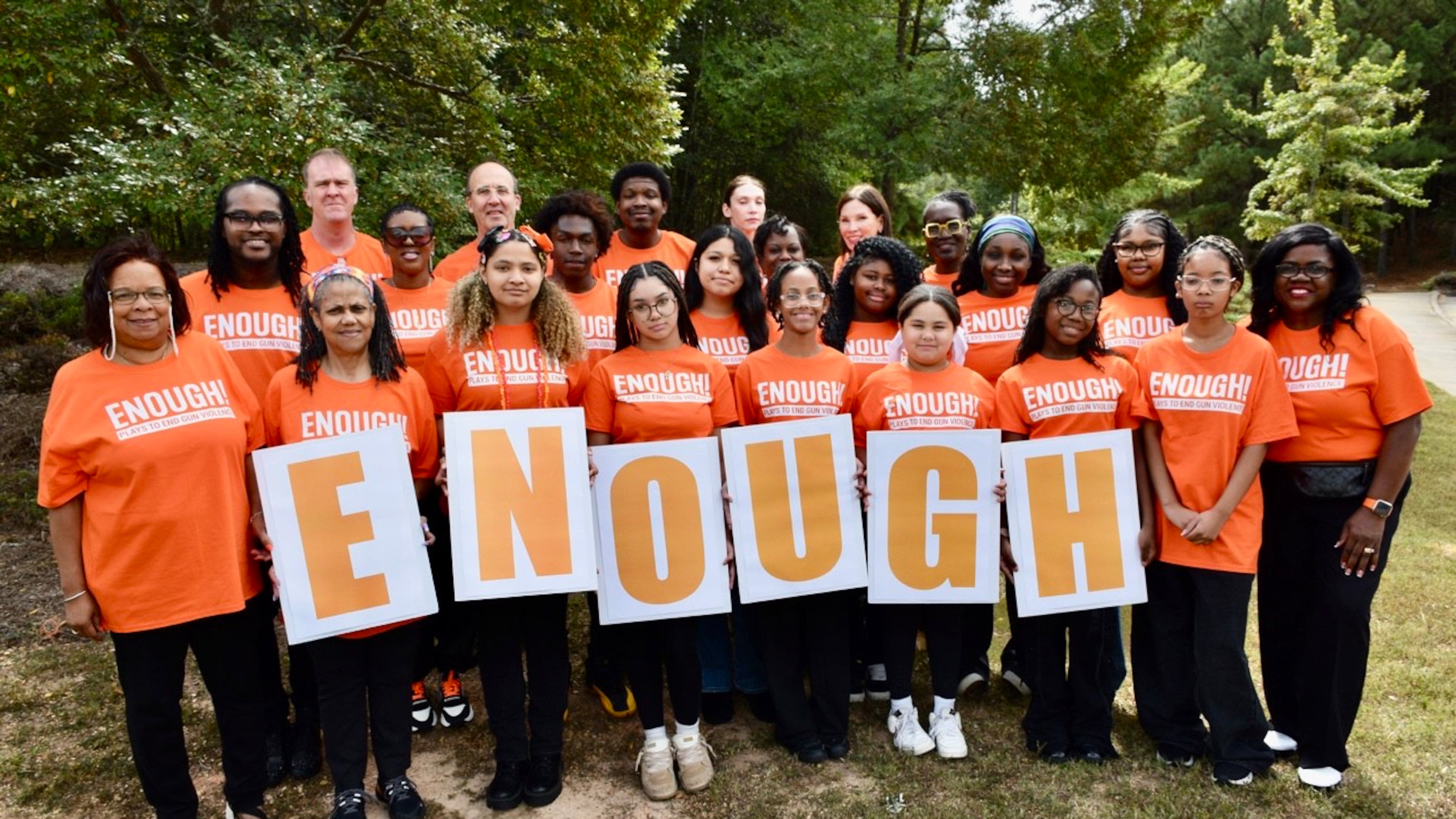 A group of peer advocates and volunteers at Atlanta's Jared's Heart of Success hold up an Enough sign during a play-reading event to confront gun violence on Saturday. Jared's Heart of Success is a nonprofit started by Sharmaine Brown, who lost her son to a stray bullet in 2015. (Courtesy)