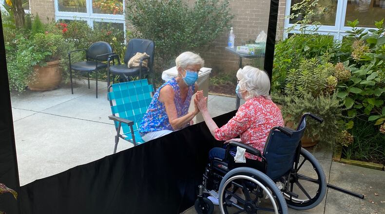 Susan Merritt, left, visits her mother, Rosie Gamel, in August at A.G. Rhodes’ Wesley Woods location. A divider is used to allow families to visits residents as safely as possible during the coronavirus pandemic. (HANDOUT)