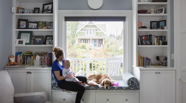 Kaitlyn Tamulonis holds daughter Julia as Kascade curls up on the window seat in the newly cozy and bright front room. The original fireplace (out of view) was maintained, but with a reskinned chimney. “We liked the aesthetic even if we didn’t use it,” says Jason Tamulonis. “But it had a hideous facade.” (Steve Ringman/Seattle Times/TNS)