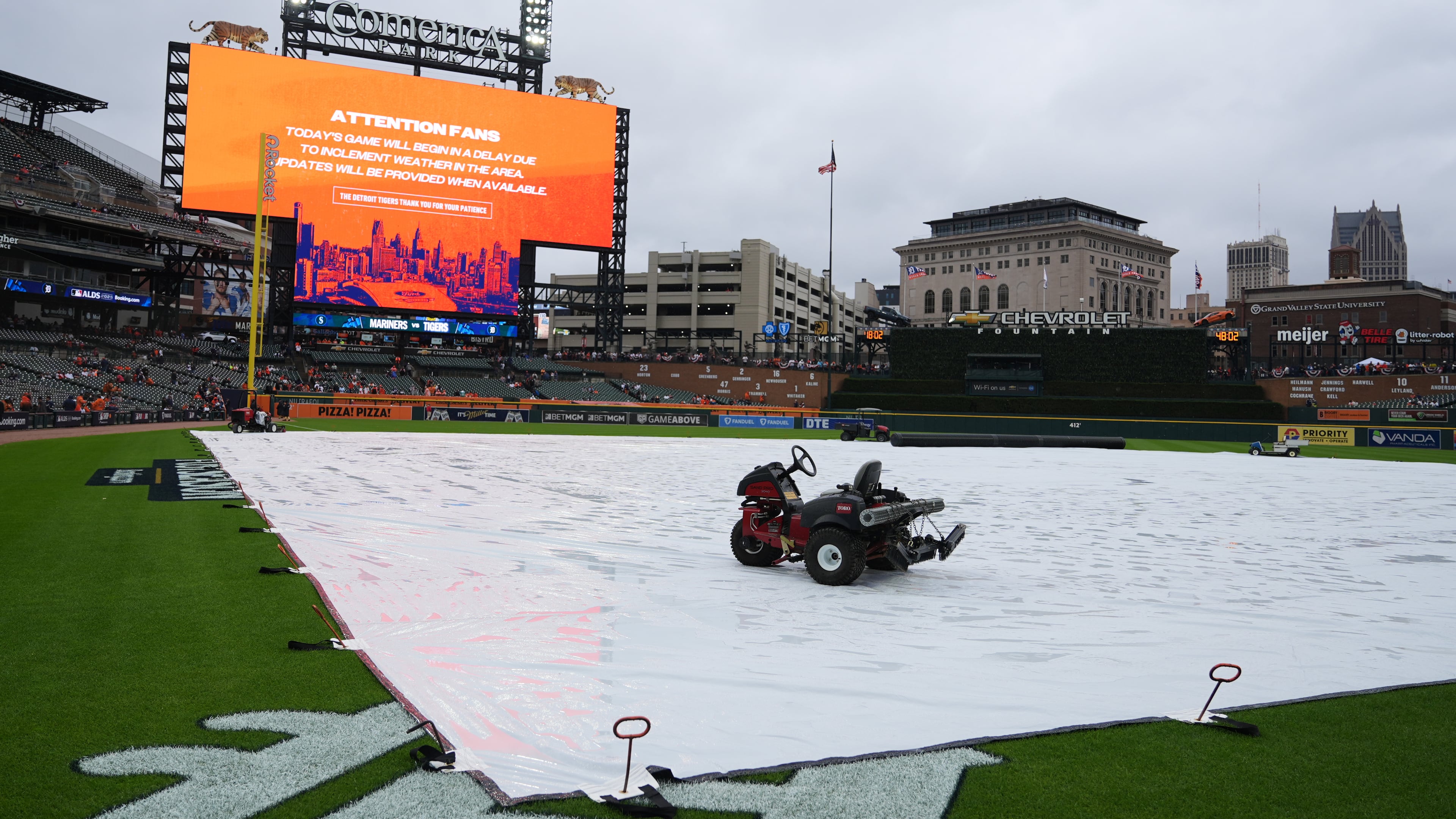 A tarp covers the field as rain falls while a message is seen on a video board alerting fans the start of Game 3 of baseball's American League Division Series between the Detroit Tigers and the Seattle Mariners will be delayed Tuesday, Oct. 7, 2025, in Detroit. (AP Photo/Ryan Sun)