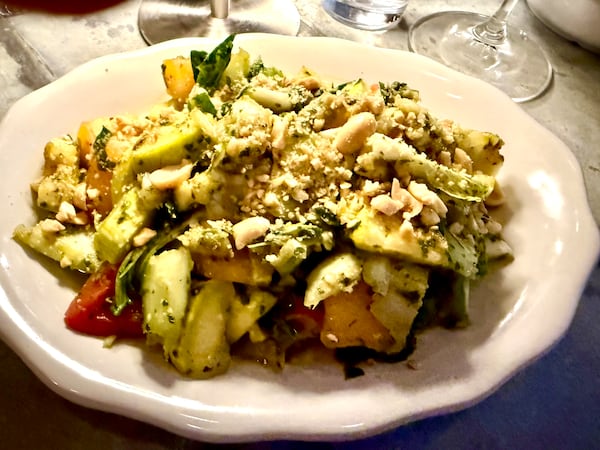 A chunky vegetable salad on a restaurant plate, topped with fresh basil and nuts