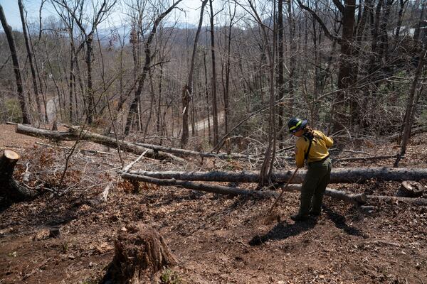A firefighter works to clear debris from Hurricane Helene to protect a home as the Black Cove Fire burns nearby Wednesday, March 26, 2025, in Saluda, N.C.. (AP Photo/Allison Joyce)