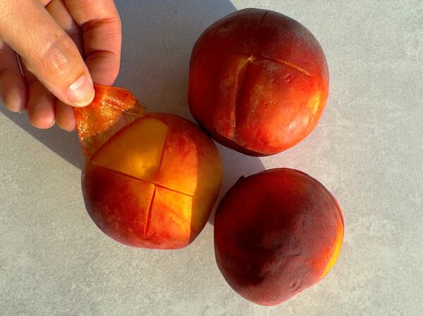 A hand peels a the skin off a peach.