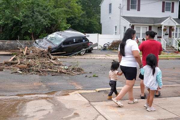 A family walks by flood-damaged cars in North Plainfield, N.J., Tuesday, July 15, 2025. (AP Photo/Seth Wenig)