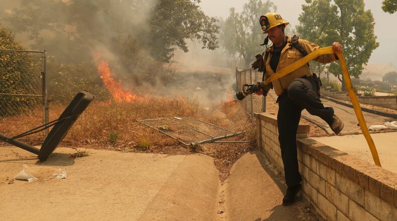 A firefighter hops over a fence while battling the Sandy Fire Monday, May 18, 2026, in Simi Valley, Calif. (AP Photo/Ethan Swope)