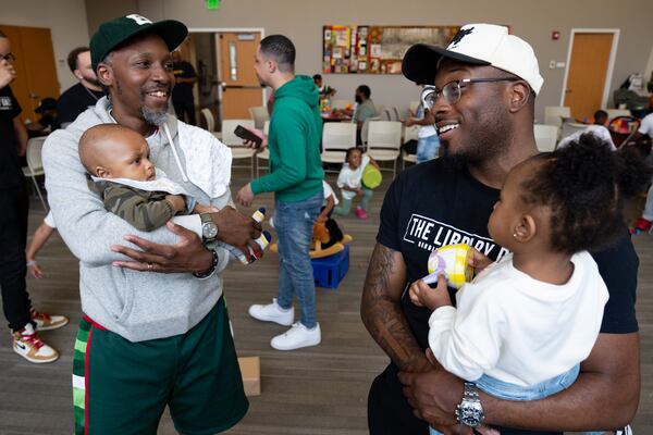 Maurice Garland (left), holding his 5-month-old son Wisdom, talks with Emmanuel Price, holding his 16-month-old daughter Harper, during a gathering of The Library Dads. The last part of each gathering is designed to encourage dads to meet and get to know each other. (Ben Gray for the AJC)