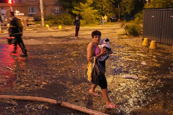 A woman carries her cat as she walks on a street at the site of a residential building that was damaged after a Russian attack, Ukraine, early Thursday, July 10, 2025. (AP Photo/Efrem Lukatsky)