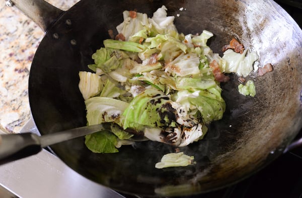 A spatula is stiring the cabbage and sauce in a wok.