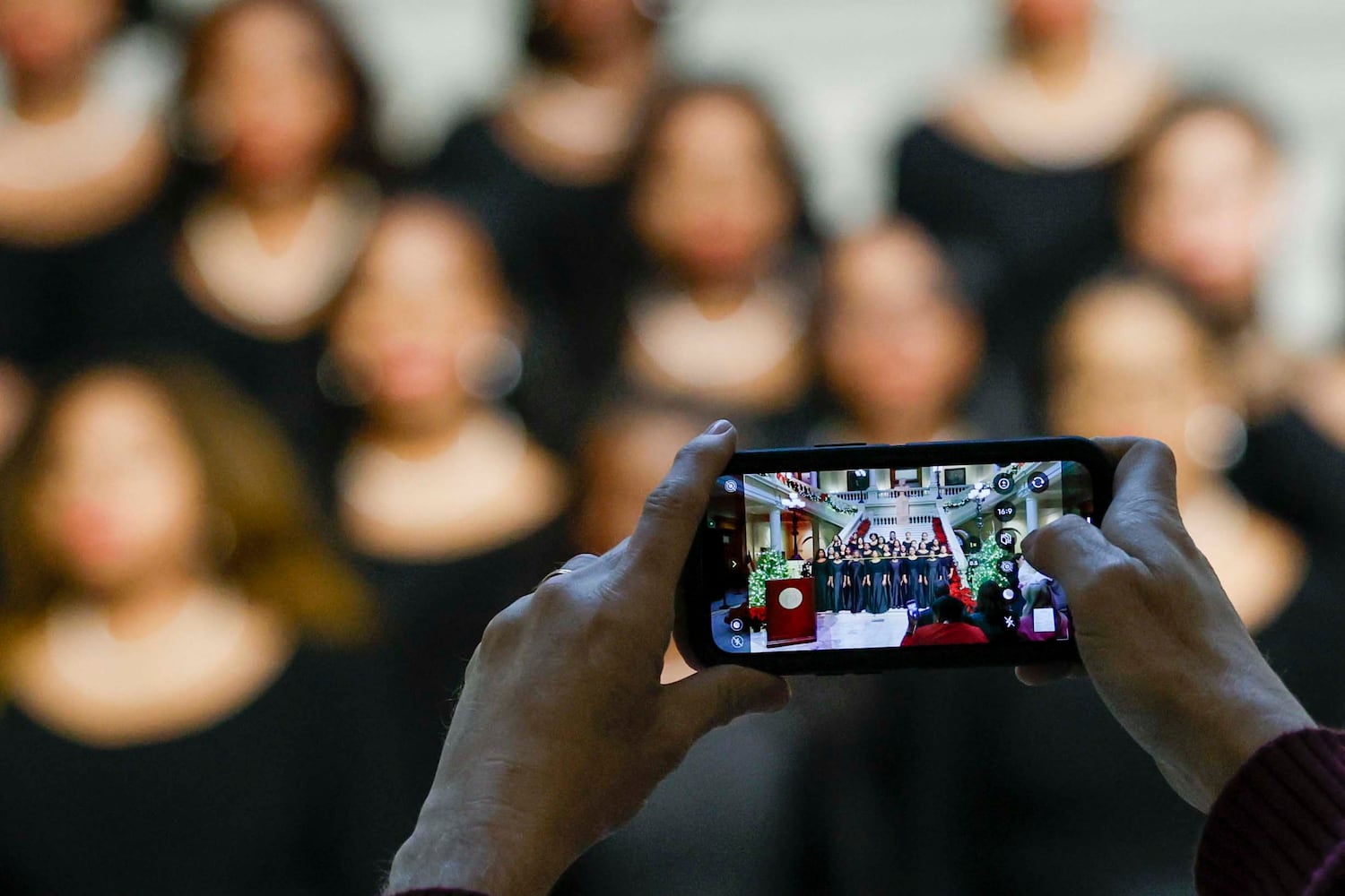 An attendee takes a cellphone photo as the Spelman Glee Club performs during the Christmas Tree Lighting ceremony at the Georgia State Capitol on Monday, Dec. 8, 2025. (Miguel Martinez/AJC)
