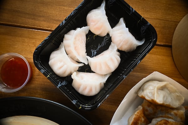 6 dumplings in a translucent wrapper, filled with shrimp, in a black takeout container.