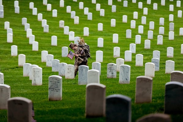 A member of the 3rd U.S. Infantry Regiment places flags at the headstones of service members buried at Arlington National Cemetery, ahead of Memorial Day, Thursday, May 22, 2025, in Arlington, Va. (AP Photo/Julia Demaree Nikhinson)