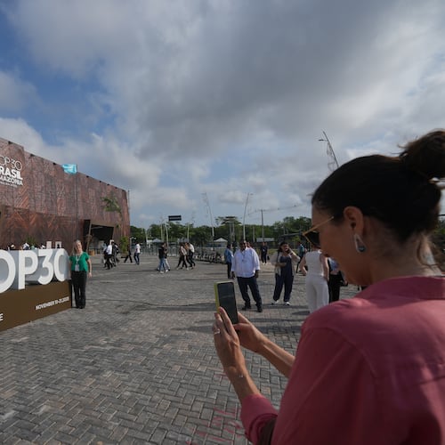 An attendee poses for a photo near a sign for the COP30 U.N. Climate Summit, Tuesday, Nov. 18, 2025, in Belem, Brazil. (AP Photo/Andre Penner)
