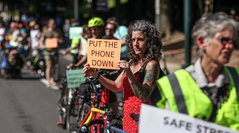 Kat Jones holds a sign during a rally on West Peachtree Street near 15th Street where William Alexander was hit and killed by a bus while riding on a scooter, Wednesday, July 24, 2019, in Atlanta. Organizers joined together as a "human protected sidewalk, bike and scooter lane" demanding the city prioritize protected bike and scooter lanes.  BRANDEN CAMP/SPECIAL