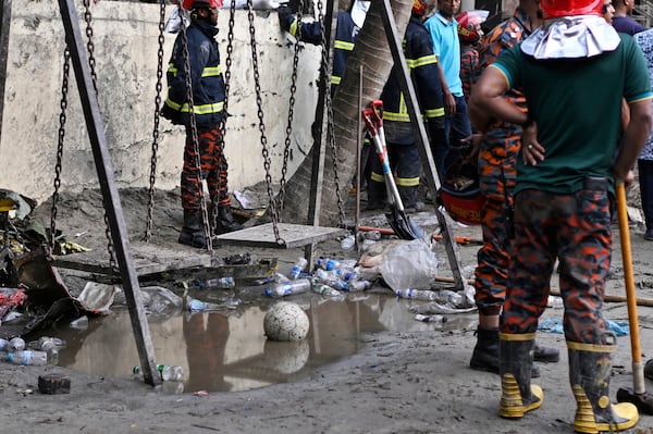 Firemen stand next to swing as they work at the site of a Bangladesh Air Force training aircraft that crashed into a school campus shortly after takeoff in Dhaka, Bangladesh, Monday, July 21, 2025. (AP Photo/Mahmud Hossain Opu)