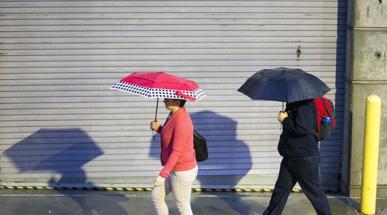 Pedestrians use their umbrellas to shield themselves from a light rain shower.